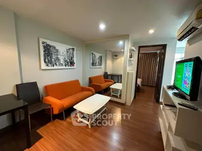 Modern living room with orange sofas, wall art, and wooden flooring in a cozy apartment.