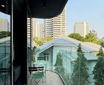 Charming balcony with glass railing offering cityscape views and cozy seating area.