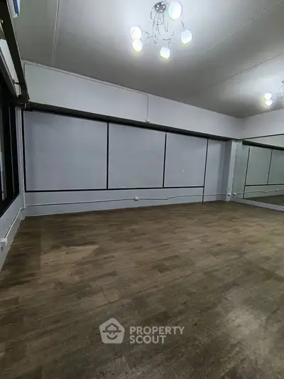 Spacious room with wooden flooring and large mirrors, ideal for dance or fitness studio.