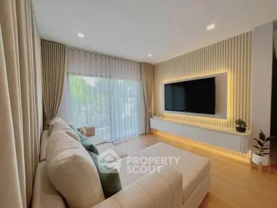 Modern living room with elegant decor and large TV, featuring cozy seating and natural light.