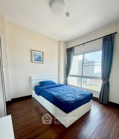 Bright bedroom with large window and city view, featuring a single bed and wooden flooring.