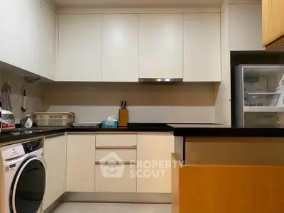 Modern kitchen with sleek cabinetry and built-in appliances, featuring a washing machine and open layout.