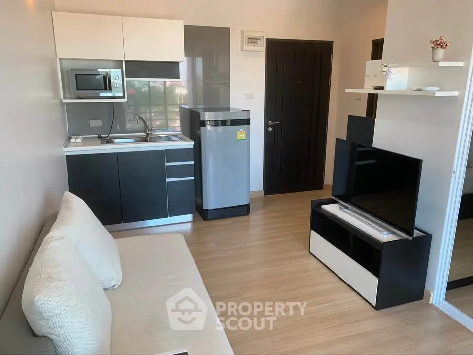 Modern compact living room with kitchenette and sleek appliances in a cozy apartment.