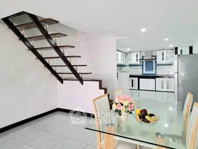 Modern open-plan kitchen and dining area with sleek staircase and glass table.