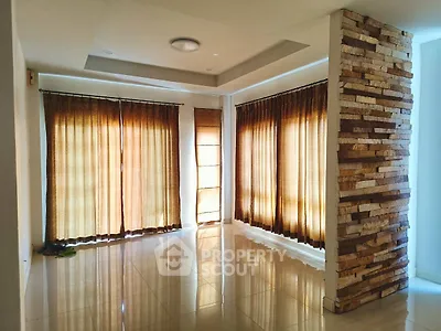 Spacious living room with large windows and stylish stone accent wall, perfect for natural light lovers.