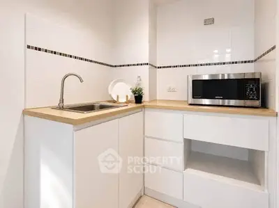 Modern kitchen with sleek white cabinets and built-in microwave, featuring a minimalist design.