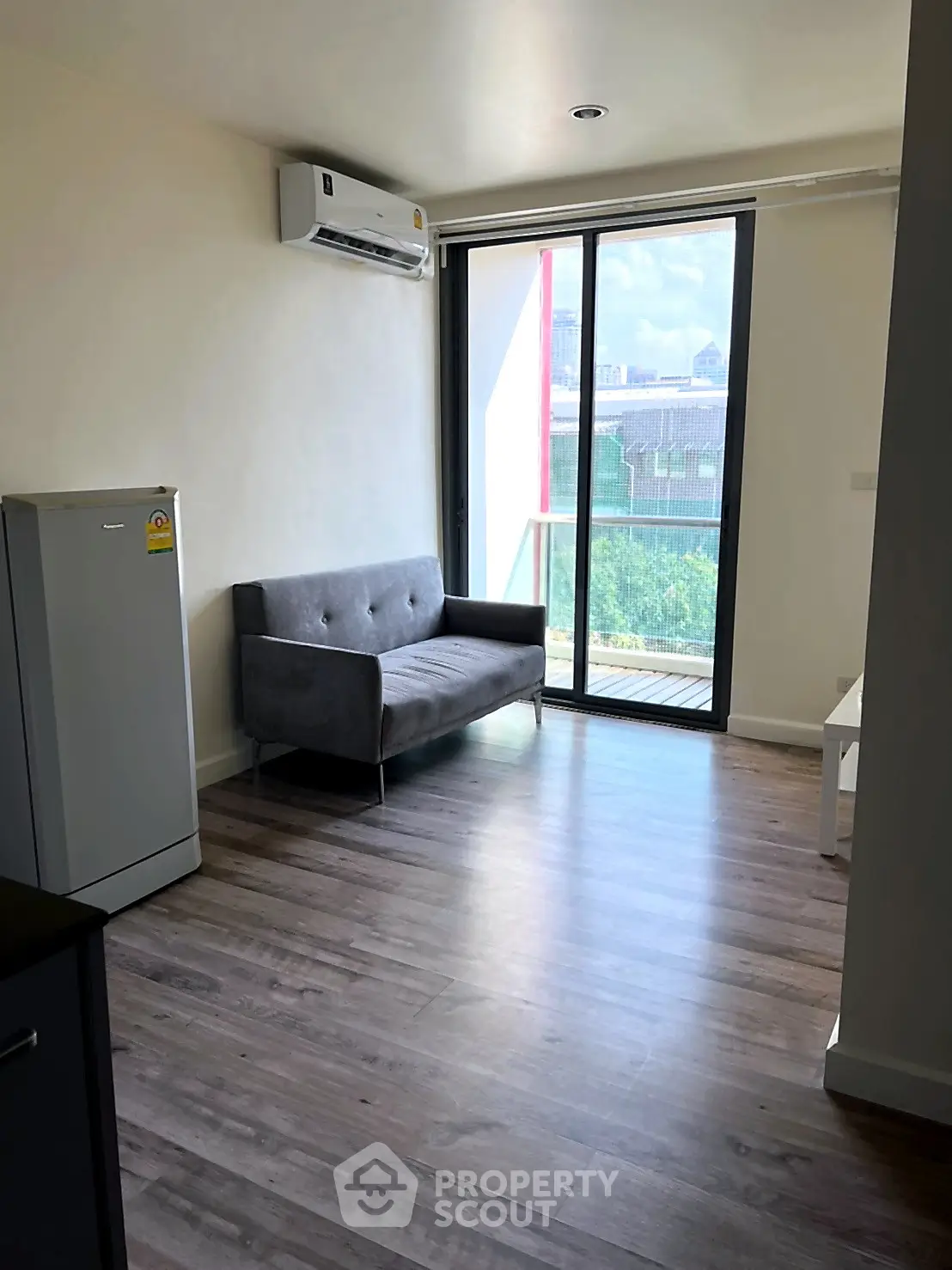 Modern living room with sleek flooring, compact sofa, and balcony view in a stylish apartment.