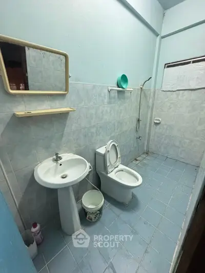 Spacious bathroom with blue tiles, featuring a toilet, sink, and shower area.