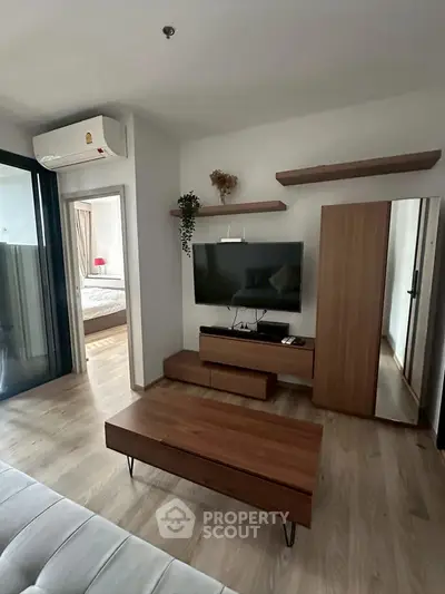 Modern living room with sleek wooden furniture and wall-mounted TV, adjacent to a cozy bedroom.