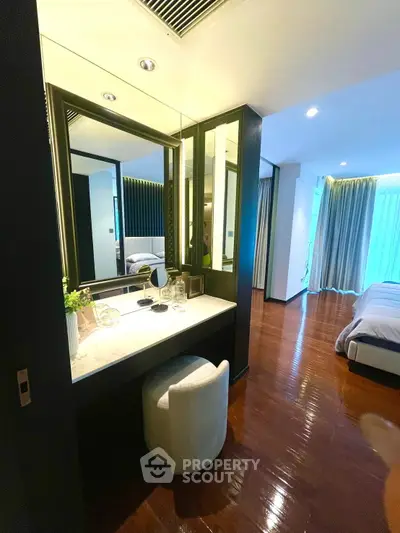 Luxurious bedroom with elegant vanity and polished wooden floors, featuring modern decor and ample natural light.