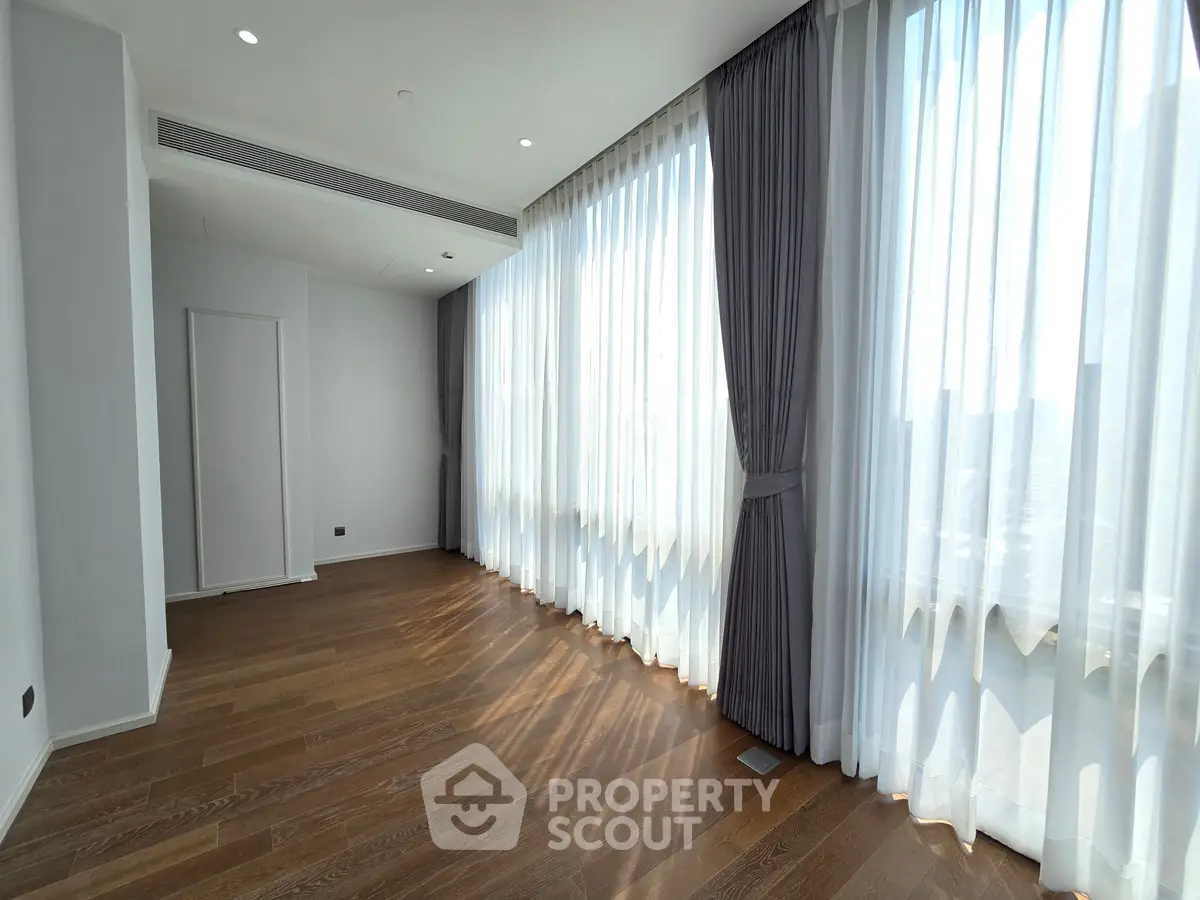 Spacious sunlit room with elegant floor-to-ceiling windows and wooden flooring, perfect for modern living.