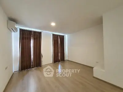 Spacious empty room with wooden flooring and large windows, perfect for customization.
