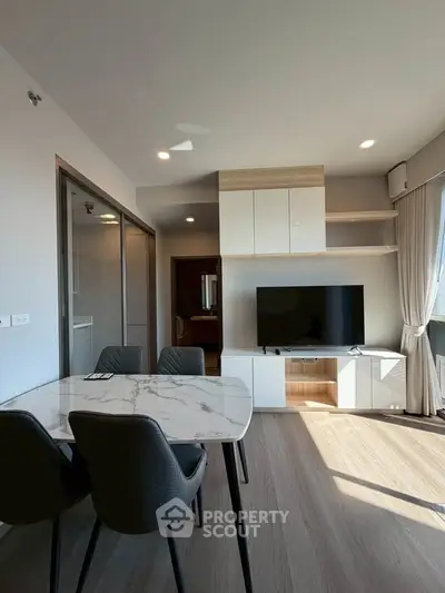 Modern living room with sleek furniture and natural light, featuring a marble dining table and built-in TV unit.