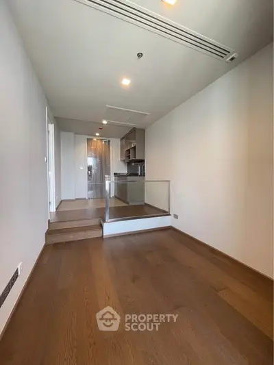 Spacious modern apartment interior with wooden flooring and open kitchen layout.