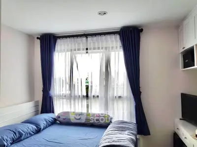 Cozy bedroom with blue curtains and bedding, featuring a window view.