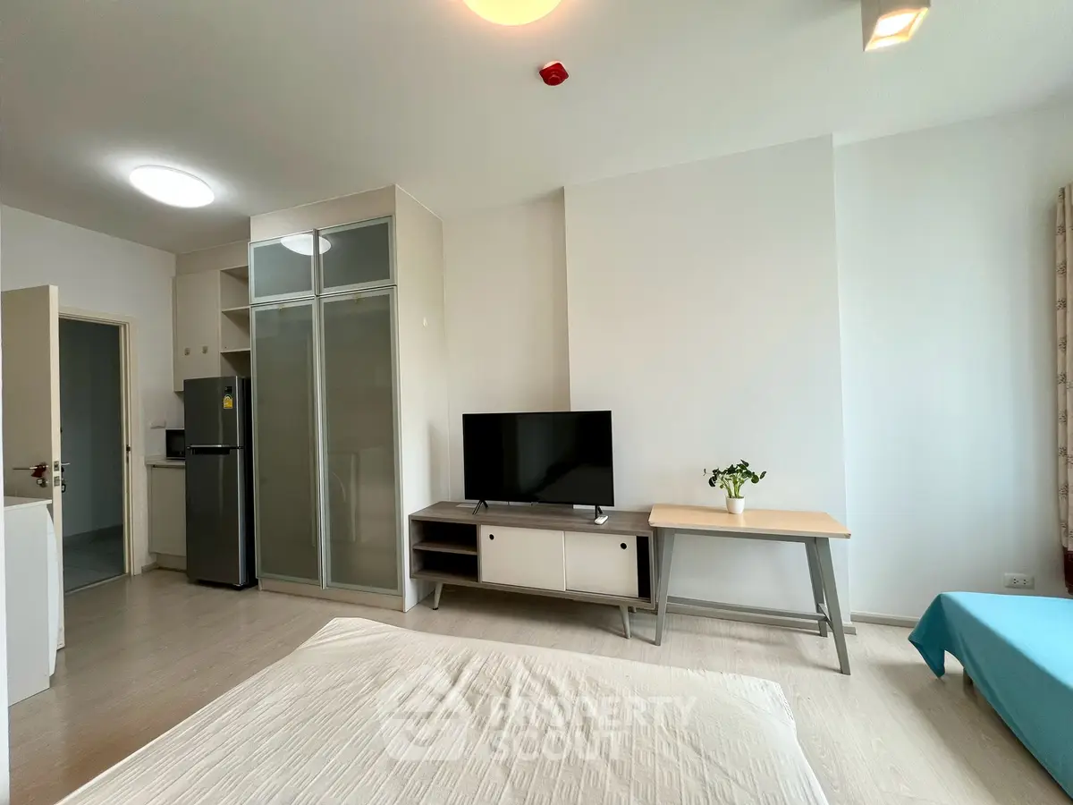 Modern studio apartment with sleek design, featuring a cozy bed, TV unit, and compact kitchen area.