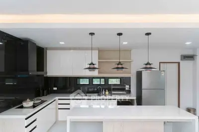 Modern kitchen with sleek design, featuring an island, pendant lights, and stainless steel appliances.