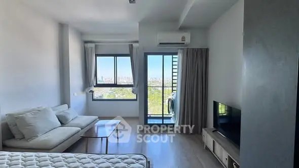 Modern living room with balcony and city view, featuring sleek furniture and natural light.