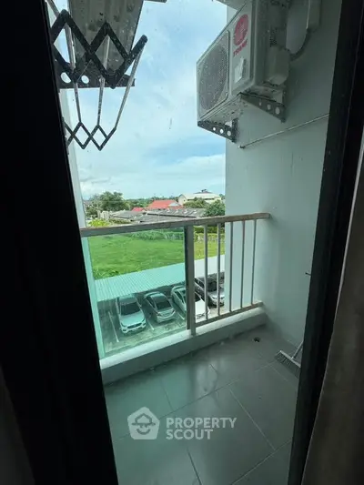 Compact balcony with air conditioning unit and view of parking area.