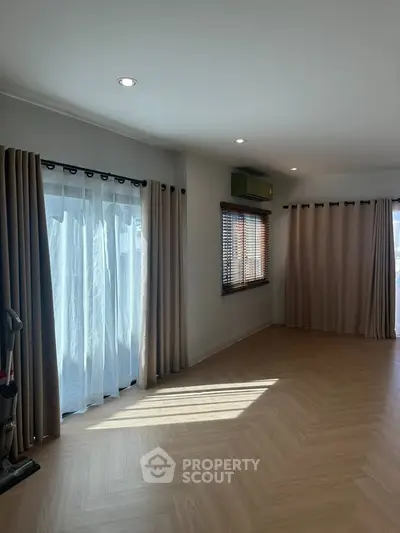 Spacious living room with large windows and elegant curtains, featuring modern lighting and hardwood flooring.