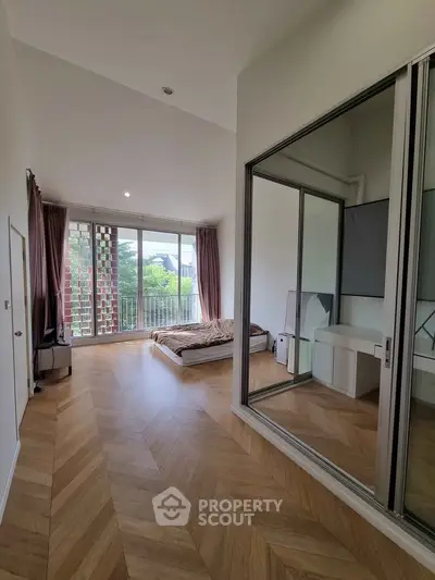 Spacious bedroom with large windows and balcony access, featuring elegant wood flooring and modern decor.
