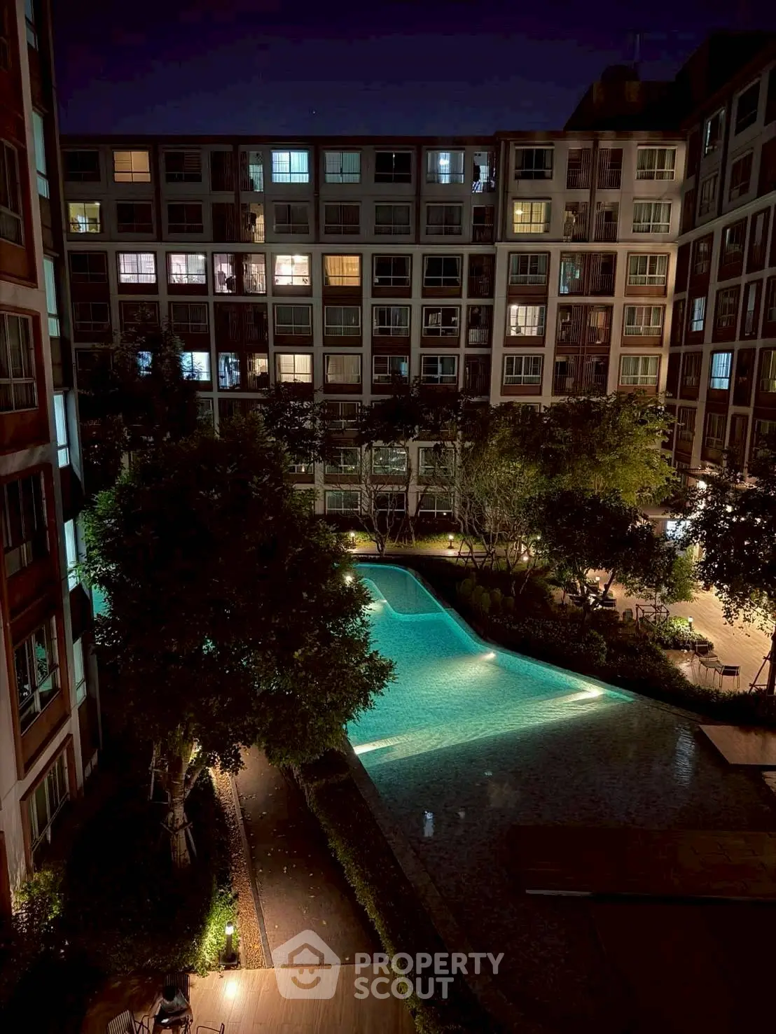 Stunning night view of modern apartment complex with illuminated pool and lush greenery.