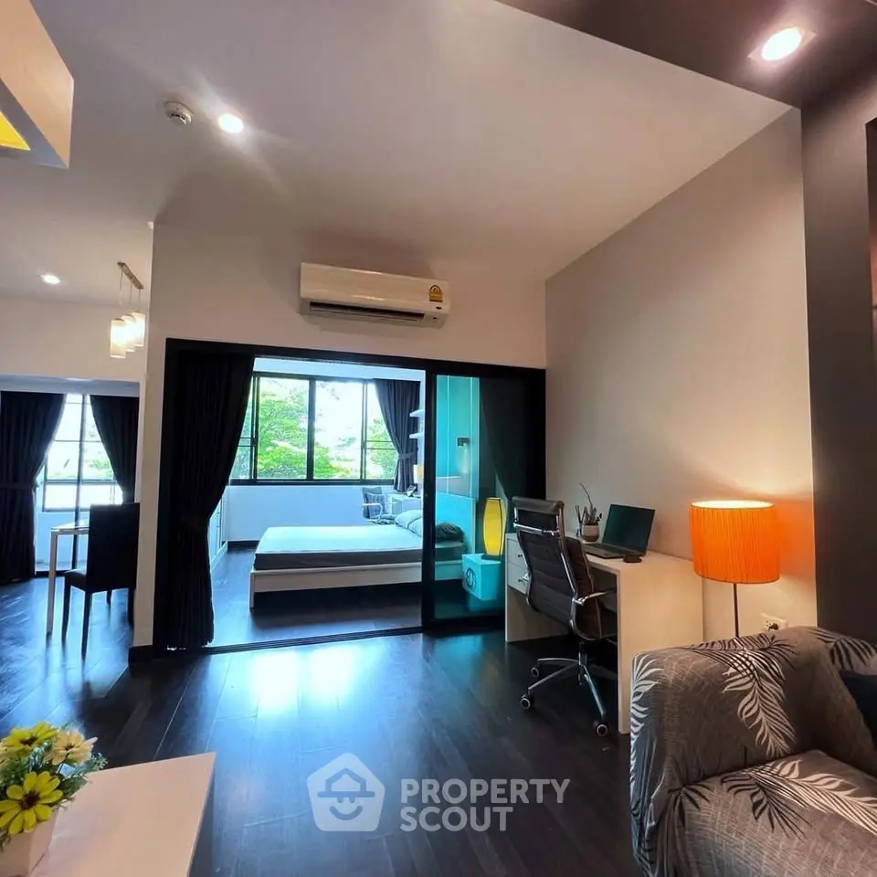 Modern open-plan living room with study area and bedroom, featuring sleek design and natural light.