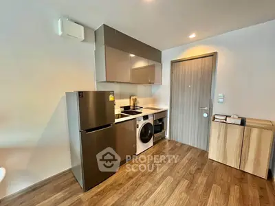 Modern kitchen with sleek appliances and wooden flooring in a compact apartment.