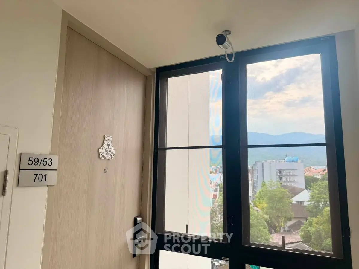 Modern apartment entrance with scenic view through large window, showcasing secure door and mountain backdrop.