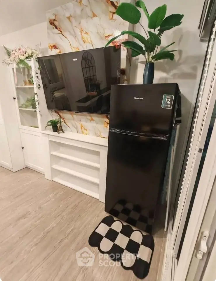 Modern living room with stylish decor, featuring a large TV and sleek black refrigerator.