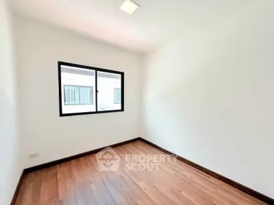 Spacious empty room with wooden flooring and large window, perfect for customization.