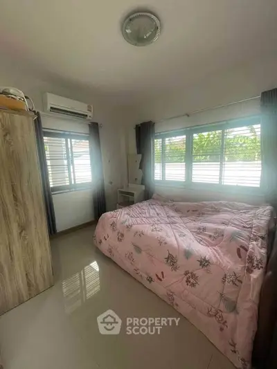Cozy bedroom with large windows and air conditioning, featuring a floral bedspread and modern wardrobe.