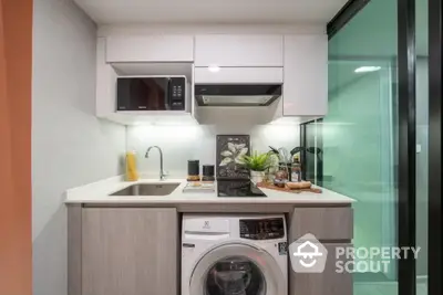 Modern compact kitchen with built-in appliances and washing machine, featuring sleek cabinetry and glass partition.