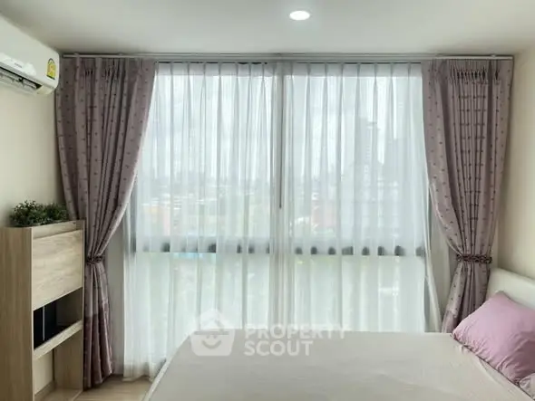 Cozy bedroom with large window and elegant curtains, offering a serene city view.