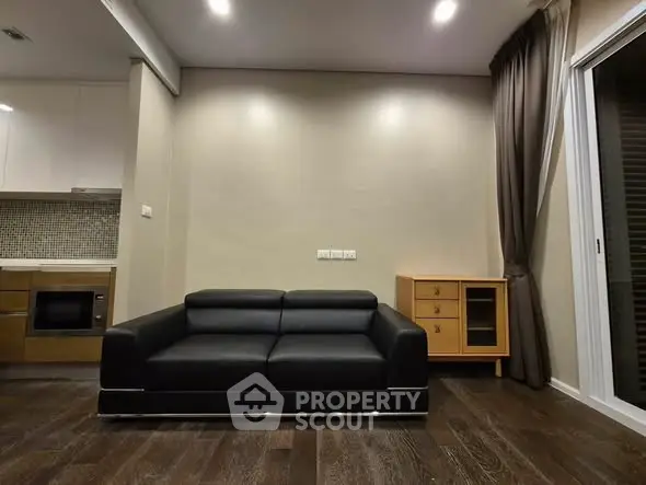 Modern living room with sleek black sofa and stylish wooden cabinet, featuring elegant dark wood flooring.