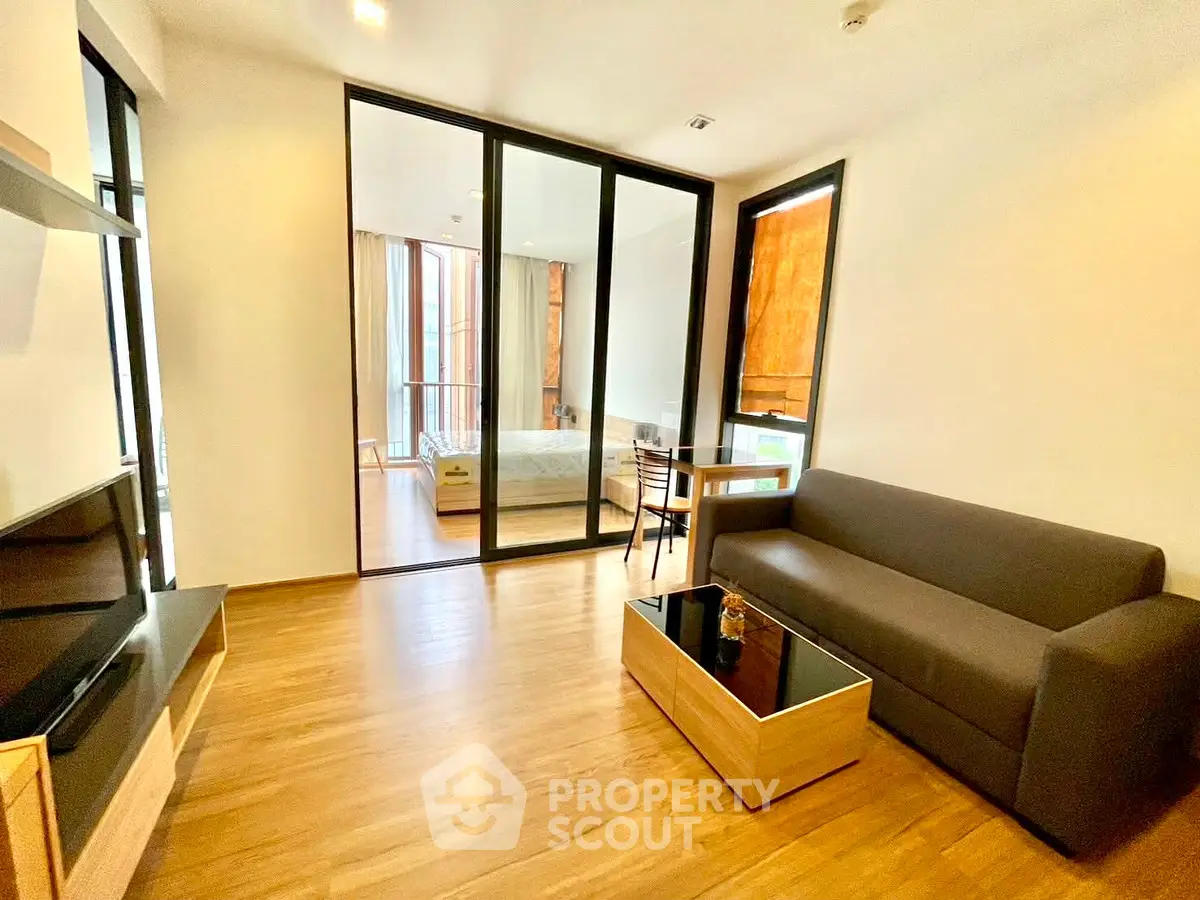 Modern living room with wooden flooring and glass partition leading to bedroom