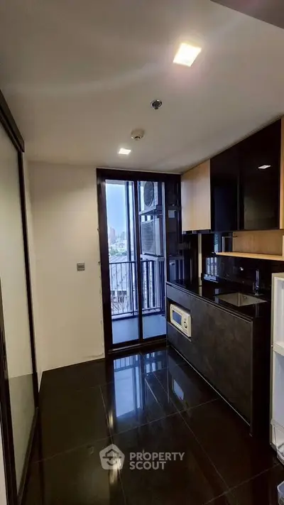 Modern kitchen with sleek black countertops and city view from balcony.