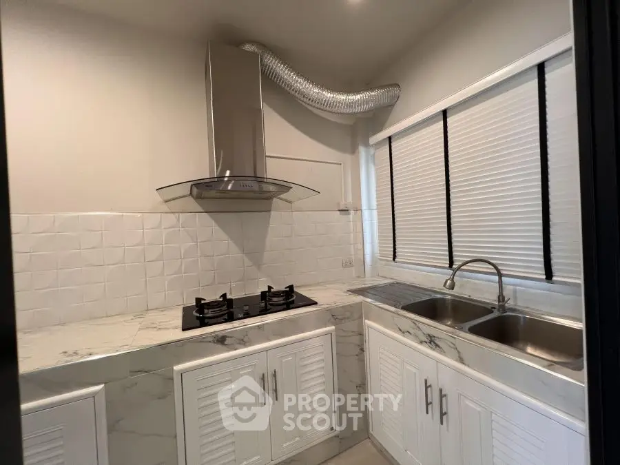 Modern kitchen with marble countertops and gas stove, featuring sleek cabinetry and dual sinks.