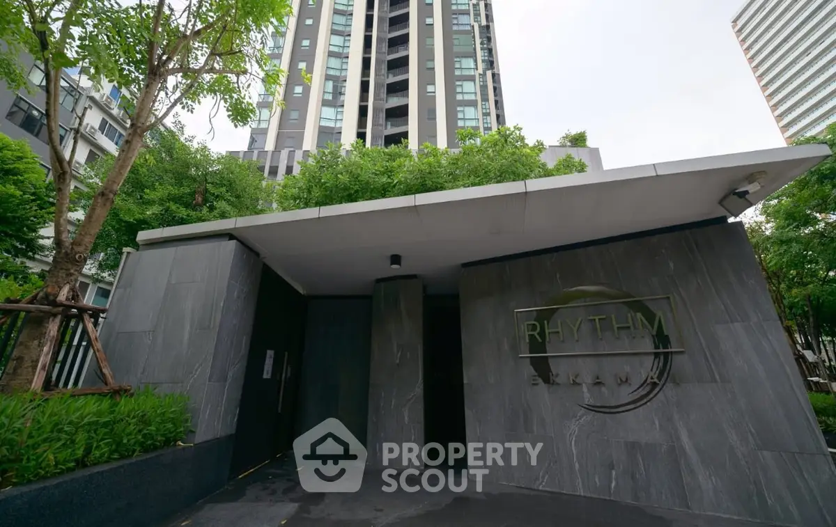 Modern high-rise building entrance with sleek design and lush greenery.