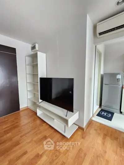 Modern living room with sleek TV stand and air conditioning, adjacent to a compact kitchen area.