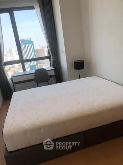 Modern bedroom with city view, featuring a comfortable bed and sleek desk setup.