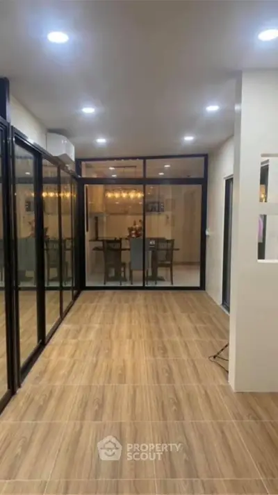 Spacious and elegantly lit living space with modern wood flooring and large glass doors leading to a cozy dining area, perfect for entertaining.