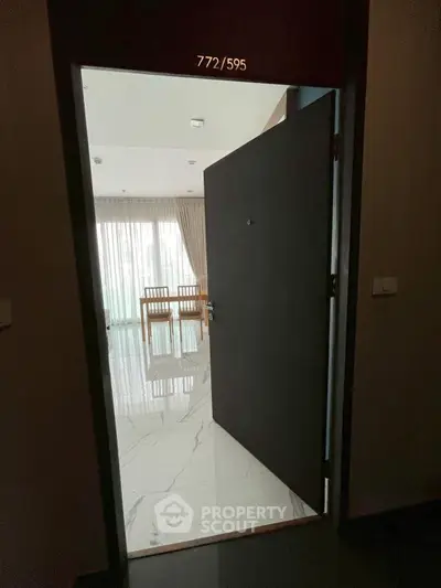 Modern apartment entrance with open door revealing elegant interior and dining area.