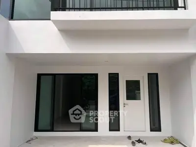 Modern minimalist white building exterior with large windows and balcony, showcasing sleek architectural design.