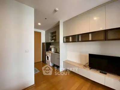 Modern apartment interior with compact kitchen and living area featuring wooden flooring.