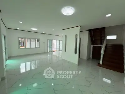 Spacious modern living room with marble flooring and staircase, ample natural light, and sleek design.