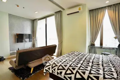 Modern bedroom with stylish decor, large windows, and a wall-mounted TV in a cozy apartment.