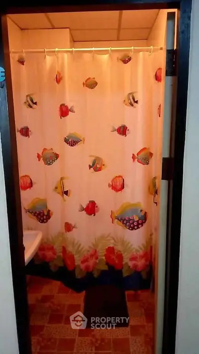 Charming bathroom with vibrant fish-themed shower curtain and cozy tile flooring.