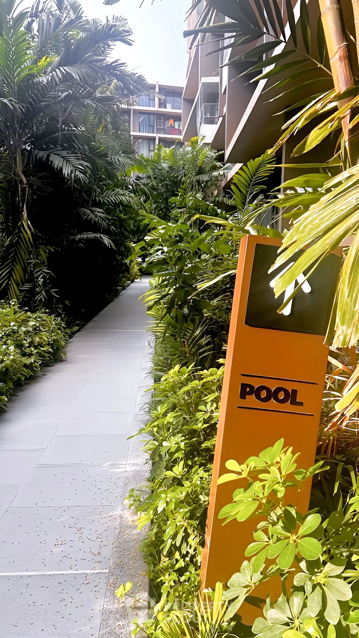 Lush garden pathway leading to a modern pool area in a luxury apartment complex.