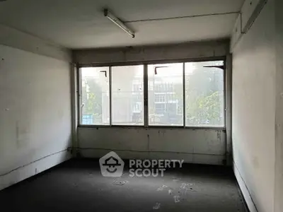 Spacious empty room with large windows and natural light, ideal for renovation.